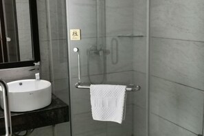 A modern bathroom with a glass shower enclosure, a white sink, and a towel rack.