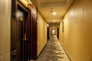 Un pasillo de hotel con piso alfombrado, puertas a la izquierda y una lámpara en el techo.