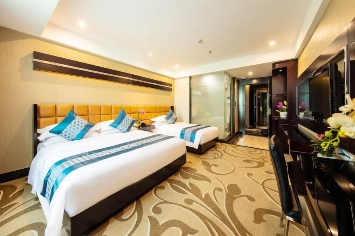 A hotel room with two beds, a TV, a desk, and a bathroom visible through a glass door.