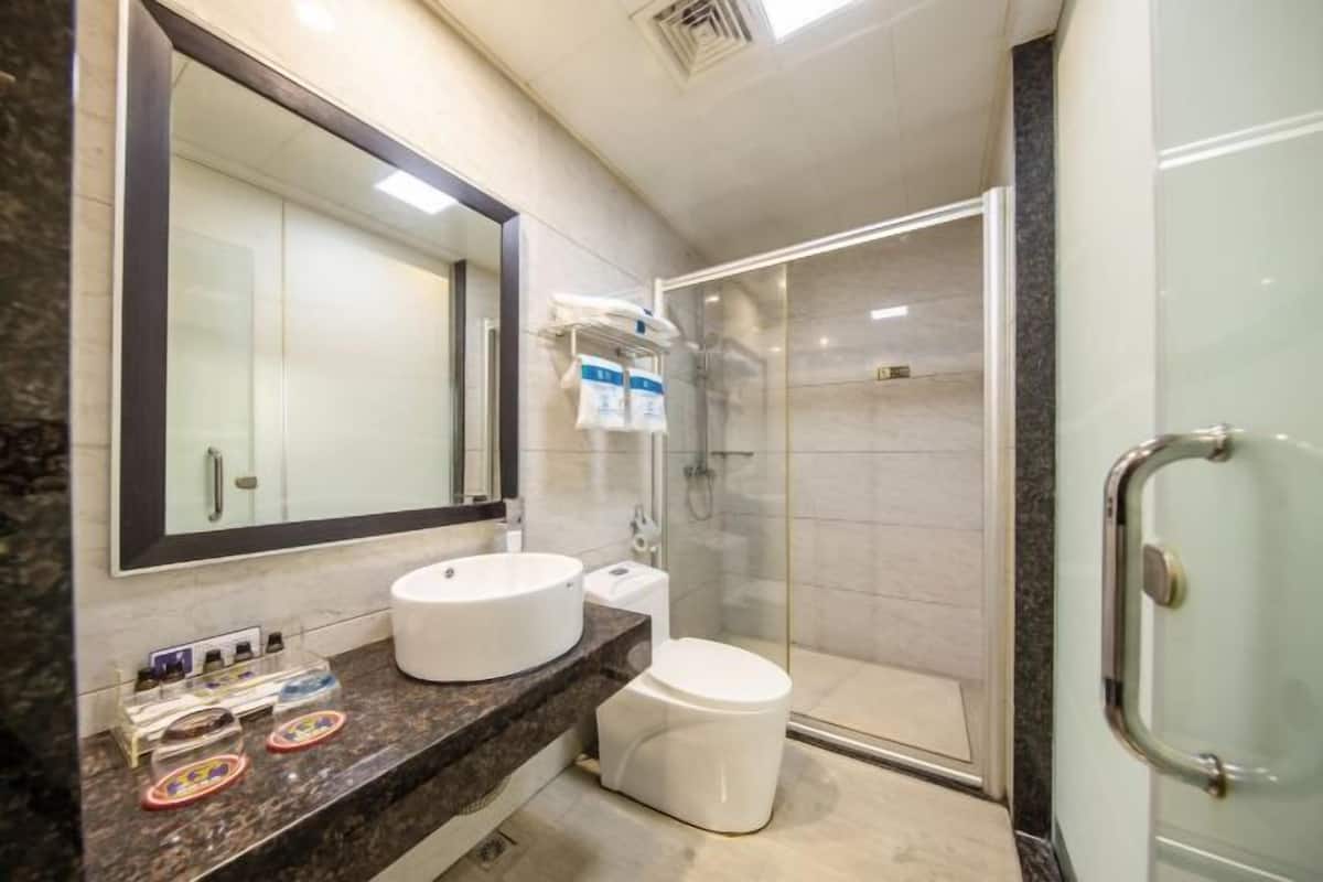 A bathroom with a large mirror, a sink, a toilet, and a glass-enclosed shower.