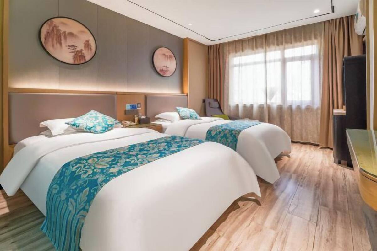 A hotel room with two beds, a desk, a chair, and a large window with curtains.