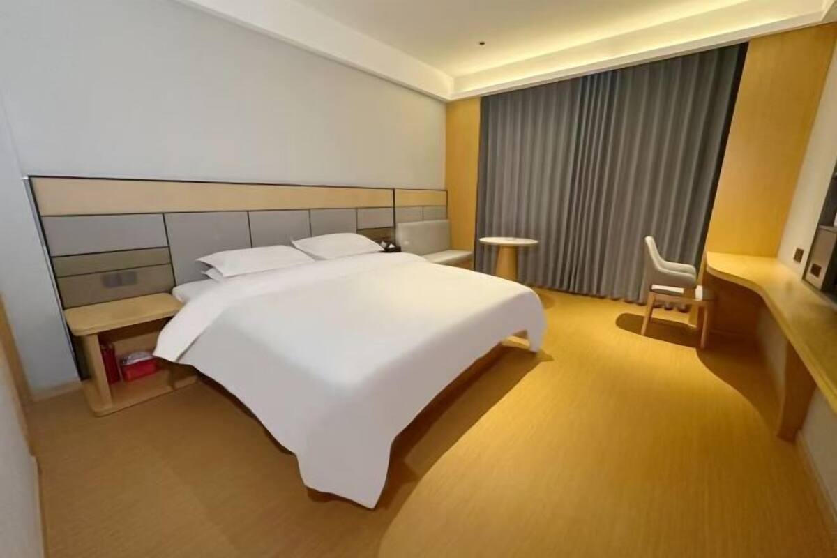 A hotel room with a bed, bedside table, chair, desk, and curtains.