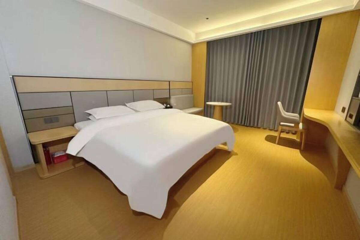 A hotel room with a large bed, a desk, a chair, and a small table.