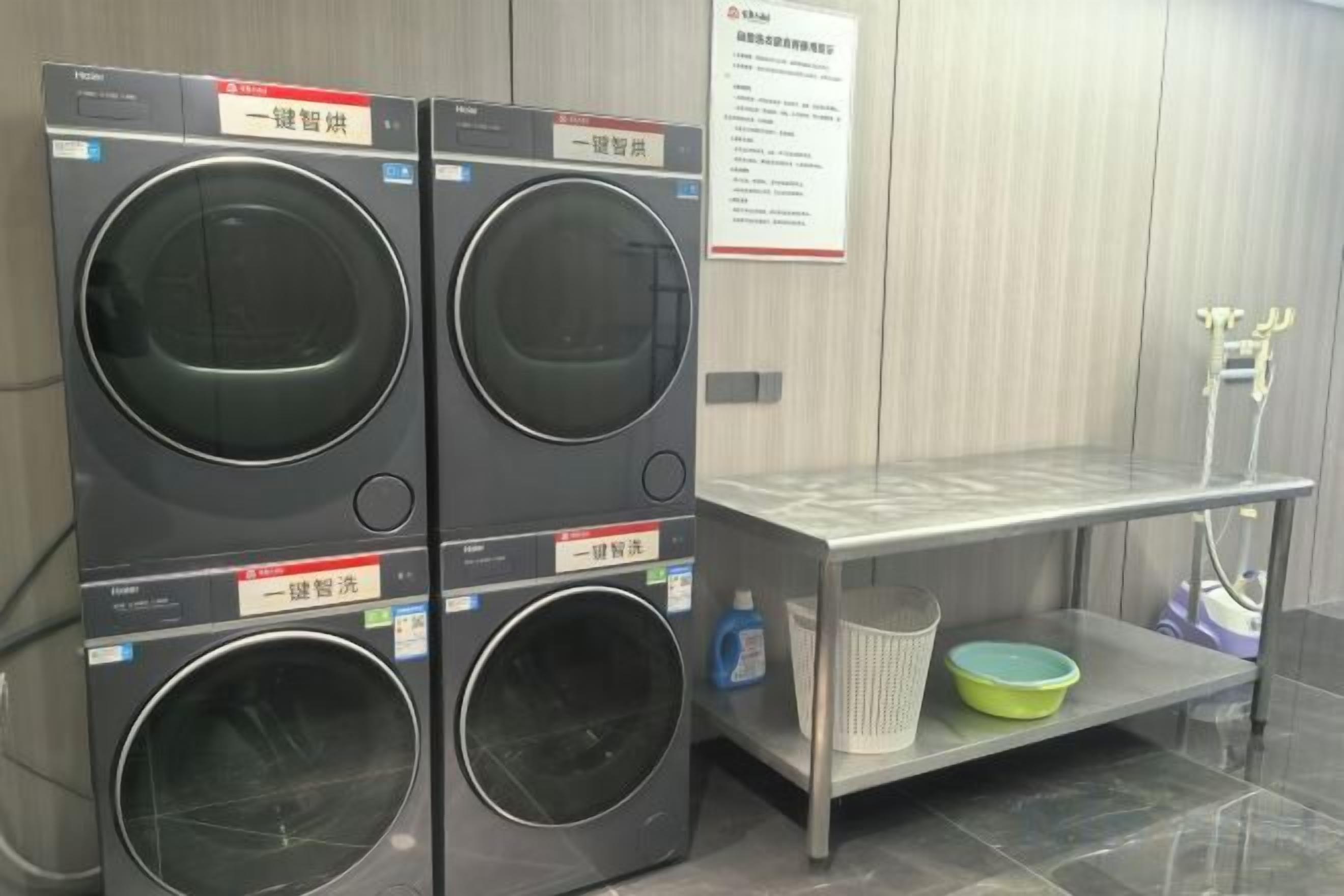 A laundry area with two stacked washing machines, a metal shelf with a green basin, and a whiteboard with text.