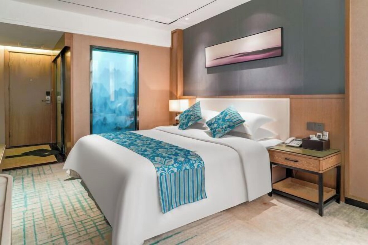 A hotel room with a bed, bedside table, and a large window.