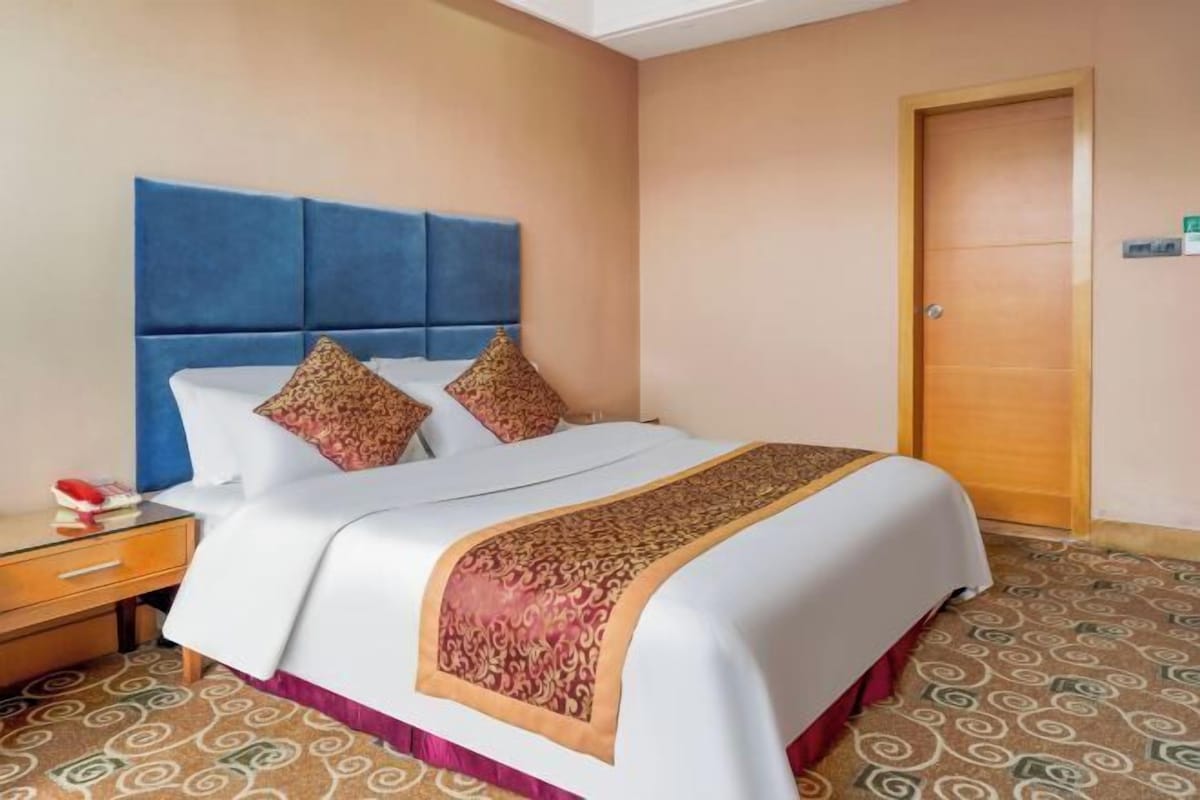 A hotel room with a large bed, a wooden nightstand, and a patterned carpet.