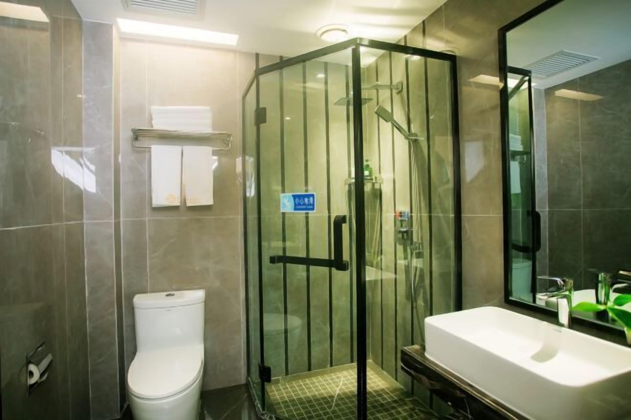 Une salle de bain moderne avec une douche à parois de verre, des toilettes blanches et un grand lavabo agrémenté d’un miroir.