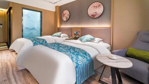 Quarto de hotel com cama, uma mesinha, uma cadeira e obras de arte nas paredes.