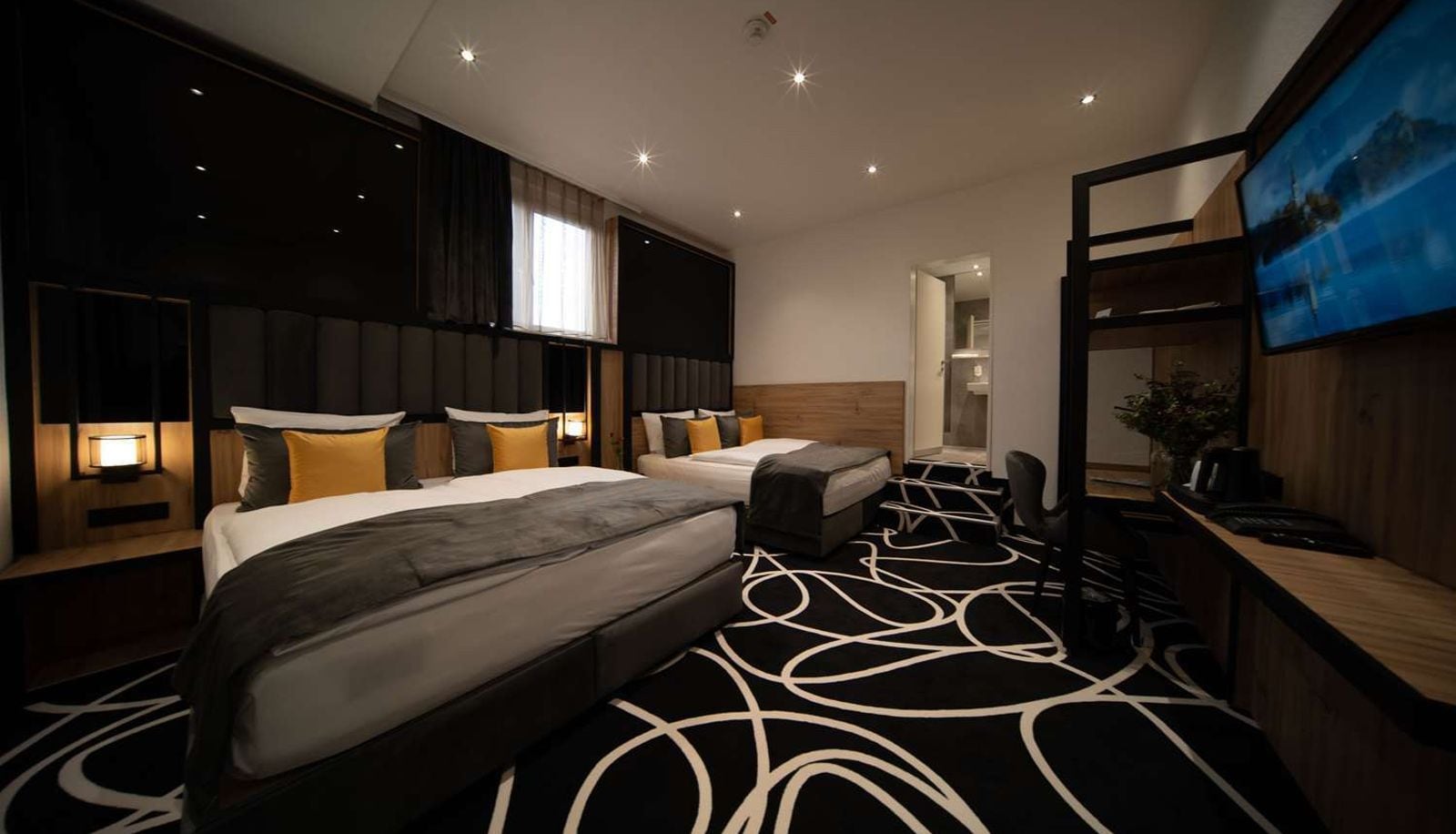 A hotel room with two beds, a desk, a TV, and a patterned carpet.