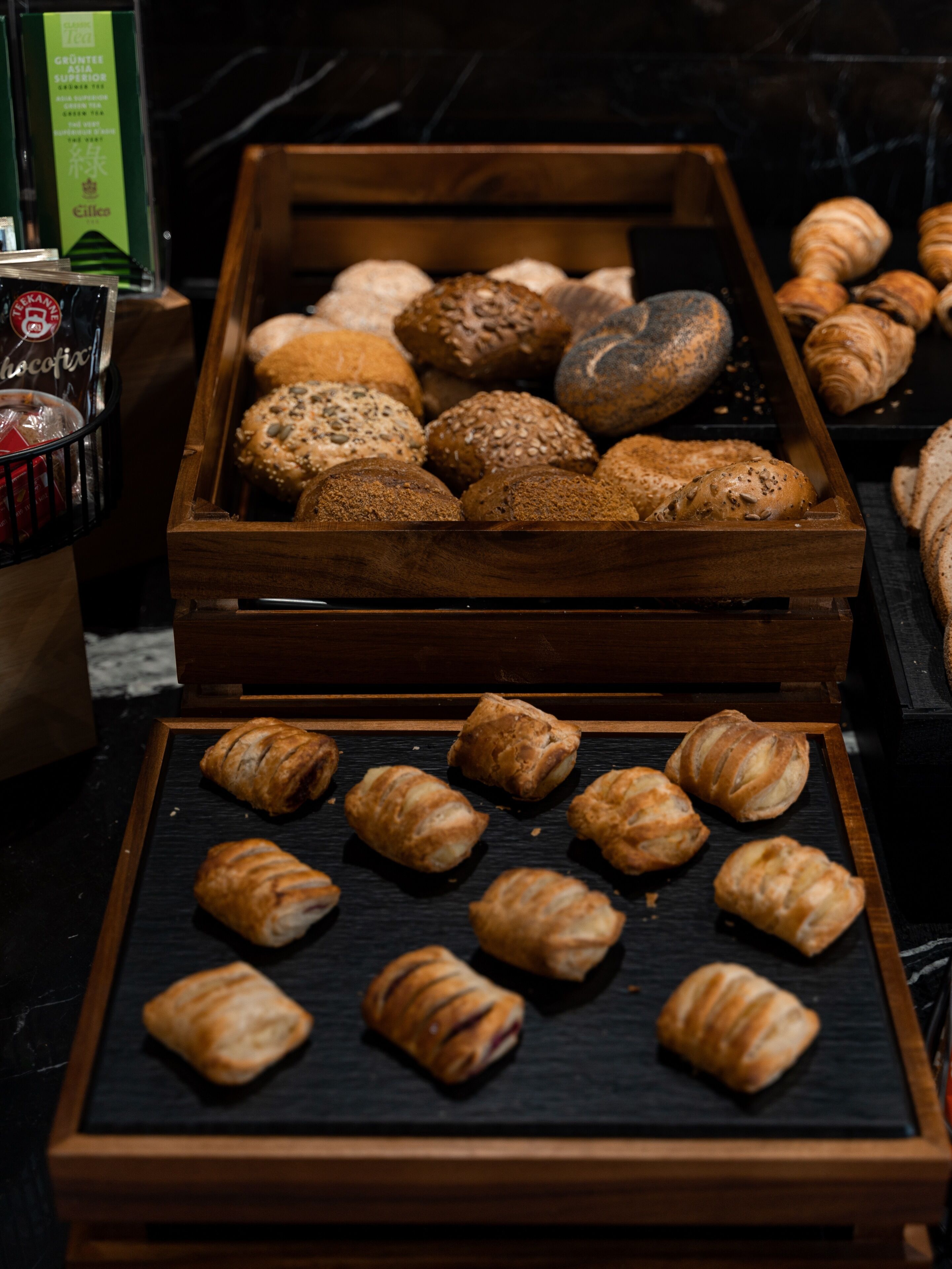 Verschiedene Backwaren, darunter Brot und Gebäck, werden in Holzeinsatzschalen präsentiert.