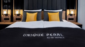 Una cama con colcha blanco y negro, dos almohadas amarillas y cabecero con listones verticales.