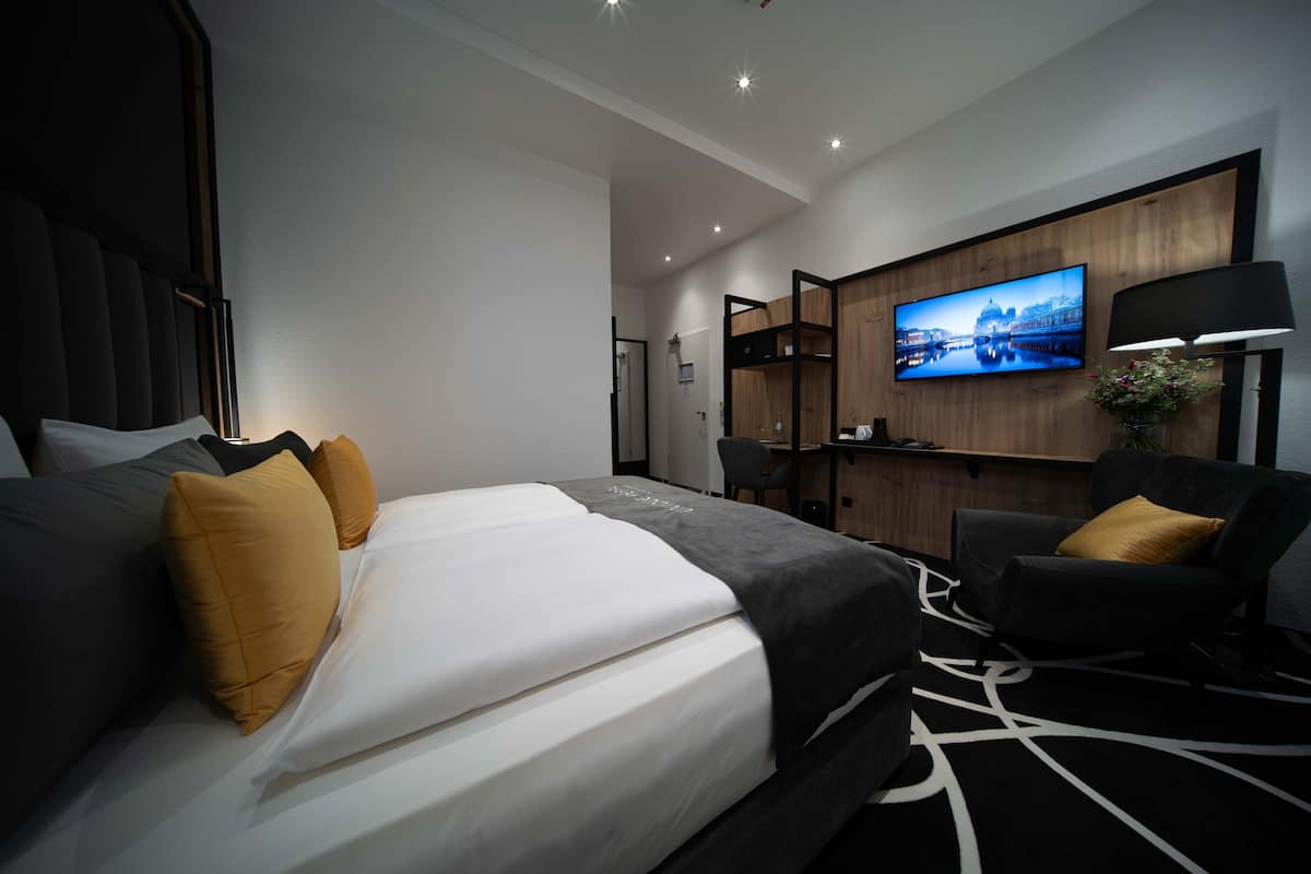Une chambre d’hôtel moderne, dotée d’un grand lit, d’un bureau, d’une chaise et d’un téléviseur fixé au mur.