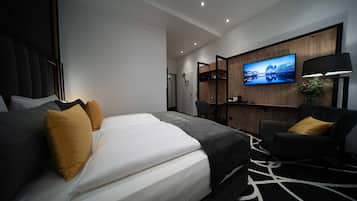 A modern hotel room with a large bed, a desk, a chair, and a TV mounted on the wall.