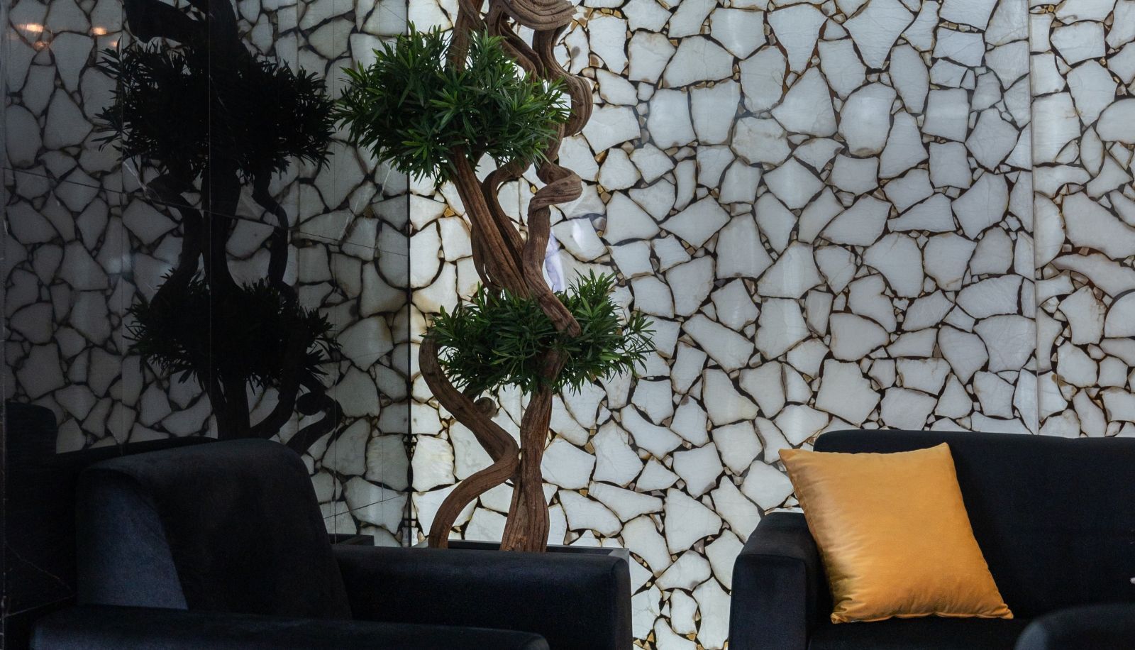 Una habitación con un sofá negro, un cojín amarillo y una pared con textura de piedra agrietada.