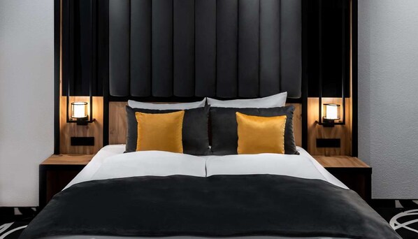 Una cama con edredón blanco y negro, dos mesitas de noche negras con lámparas y un cabecero negro con listones verticales.