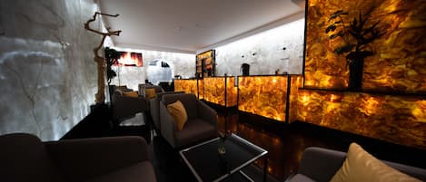 Un espace de détente moderne, avec des canapés, une table basse et un mur décoratif orné d’un arbre et de motifs abstraits.