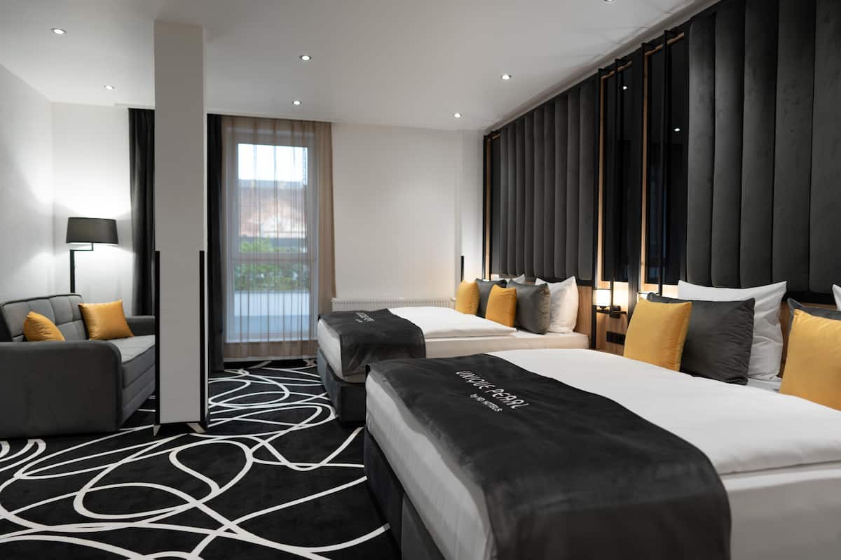 Une chambre d’hôtel moderne avec deux lits, un canapé, un bureau et une grande fenêtre avec des rideaux.