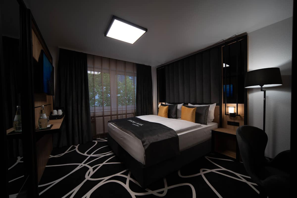 Une chambre d’hôtel moderne, dotée d’un grand lit, d’un bureau avec une lampe et offrant une vue sur l’extérieur par la fenêtre.