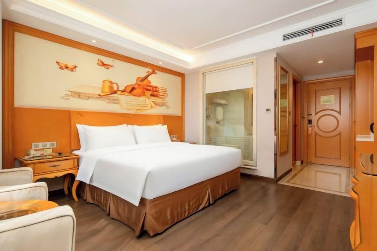 A hotel room with a large bed, a nightstand, a wall-mounted artwork, and a door leading to a bathroom.