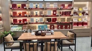 Una tienda ordenada con estanterías exhibiendo diversos productos, una mesa de madera con sillas y una planta en maceta.