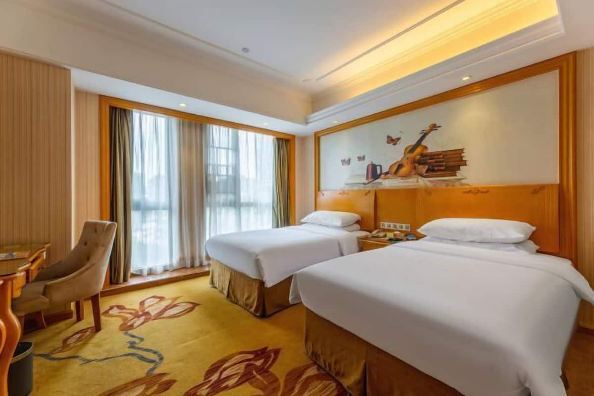 Une chambre d’hôtel avec deux lits, un bureau, une chaise et une grande fenêtre avec des rideaux.