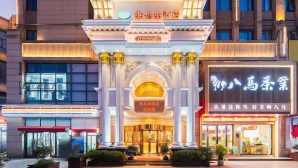 Fachada de hotel con un arco destacado, un letrero de restaurante y buena iluminación.