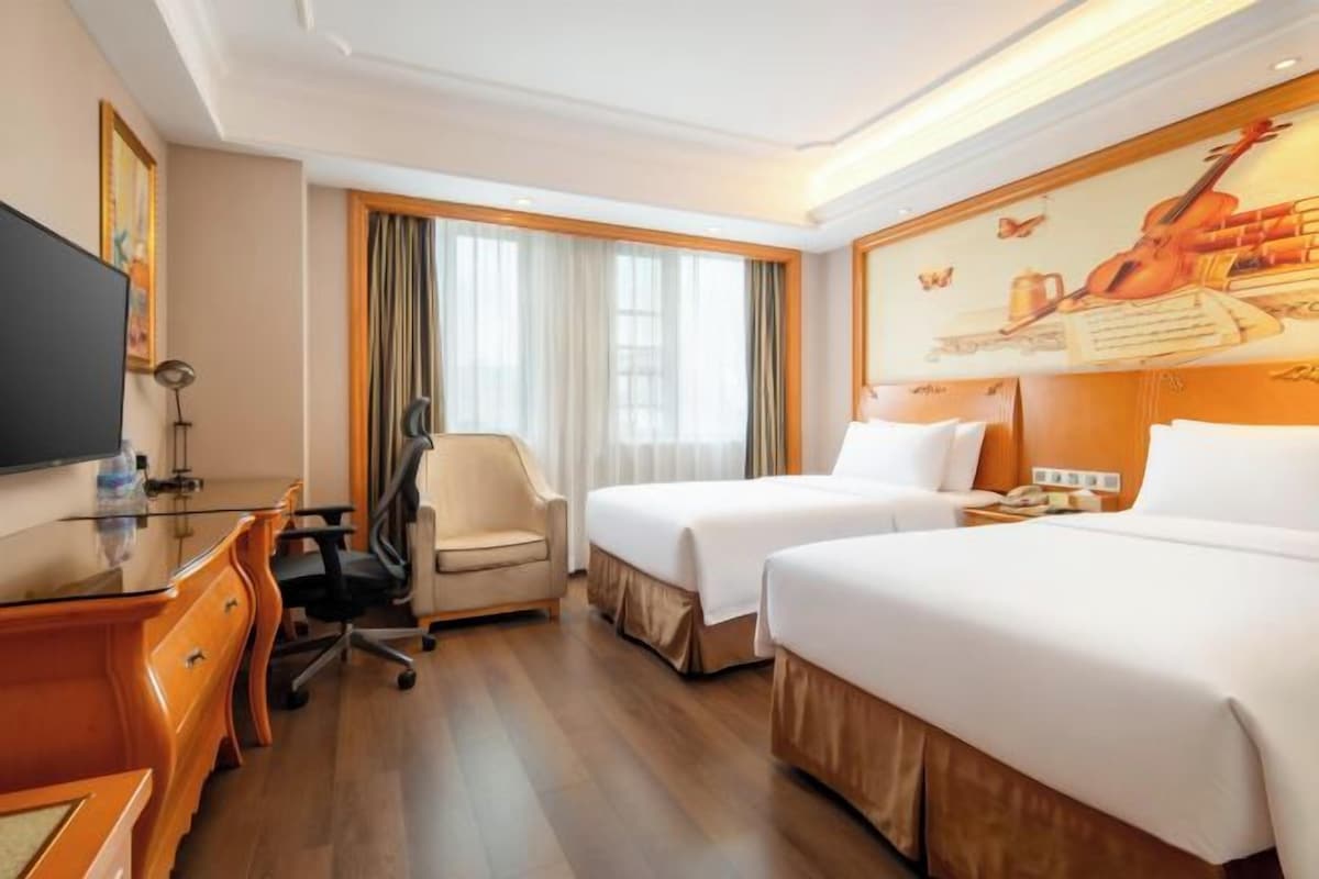 A hotel room with two beds, a desk, a chair, a television, and a large painting on the wall.