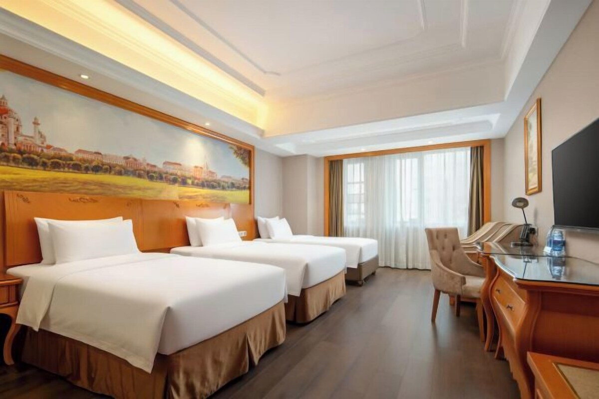 A hotel room with two beds, a desk, and a large painting on the wall.