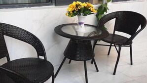 Una mesa redonda de vidrio con dos sillas negras de mimbre, un jarrón con flores amarillas y una pared blanca al fondo.