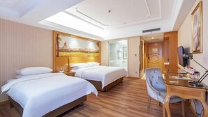 Habitación de hotel con dos camas, un escritorio, una silla, un televisor y un cuadro en la pared.