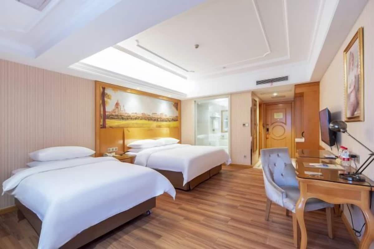 Une chambre d’hôtel avec deux lits, un bureau, une chaise, une télévision et un tableau au mur.