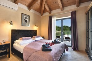 A bedroom with a large bed, a nightstand, a headboard, a framed picture, a window with curtains, and a view of the outdoors. - Villa Azur (Istria - Muntic) (Muntic)