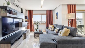 Ein modernes Wohnzimmer mit Flachbildfernseher, grauem Sofa und Couchtisch.