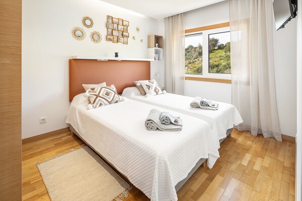 Habitación de hotel con dos camas, suelo de madera, un ventanal con vistas y decoración en las paredes.