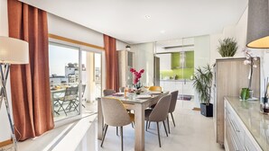 Ein moderner Essbereich mit einem Glastisch, Stühlen und Blick auf die Stadt durch große Fenster.