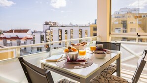 Ein Balkon mit einem Tisch, der für ein Frühstück gedeckt ist, mit Früchten, Brot und Orangensaft.