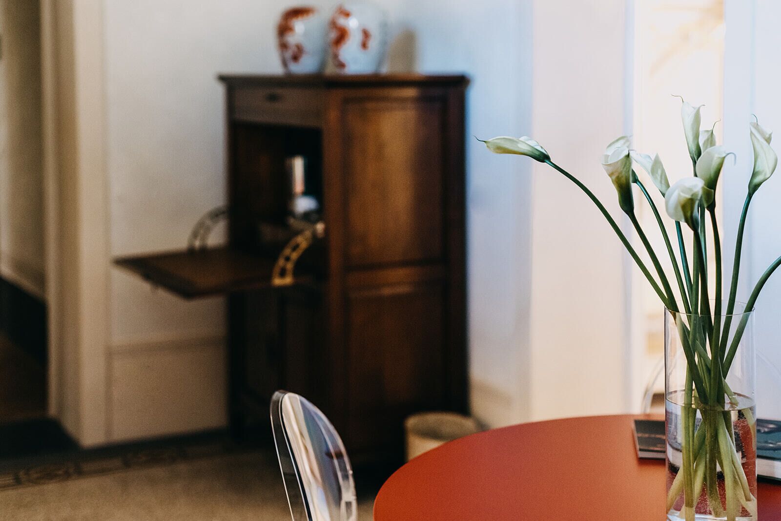 Un comedor con una mesa y sillas, un jarrón con flores y un mueble de madera al fondo.