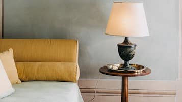 Una habitación con una cama, una mesa redonda con una lámpara y dos cuadros en la pared.