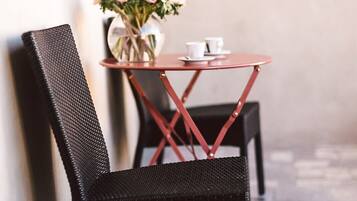 Una silla de mimbre negra y una mesita redonda con un florero y dos tazas blancas.