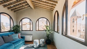 A cozy room with a blue sofa, two potted plants, and a view of historic buildings through large arched windows. - Palazzo Feroci (Pisa)