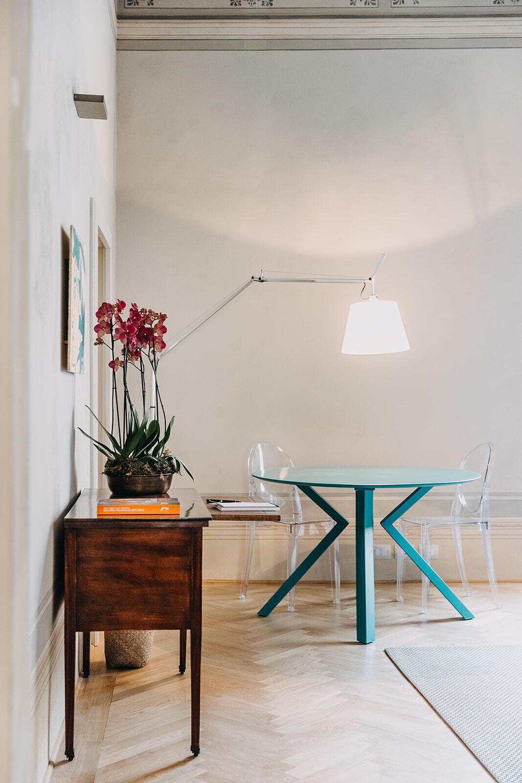 A modern interior with a wooden sideboard, a glass table with teal legs, and a clear chair.