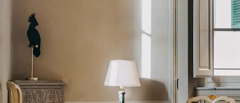 Une pièce avec une cheminée, une table avec une lampe, deux chaises et une fenêtre avec des stores.