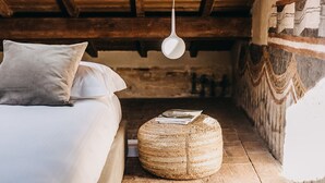 A rustic bedroom with a bed, pillows, a hanging light fixture, and a woven ottoman with magazines. - Palazzo Feroci (Pisa)