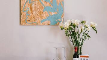 A wooden dresser with a book, wine glasses, a bottle, and a vase with flowers.