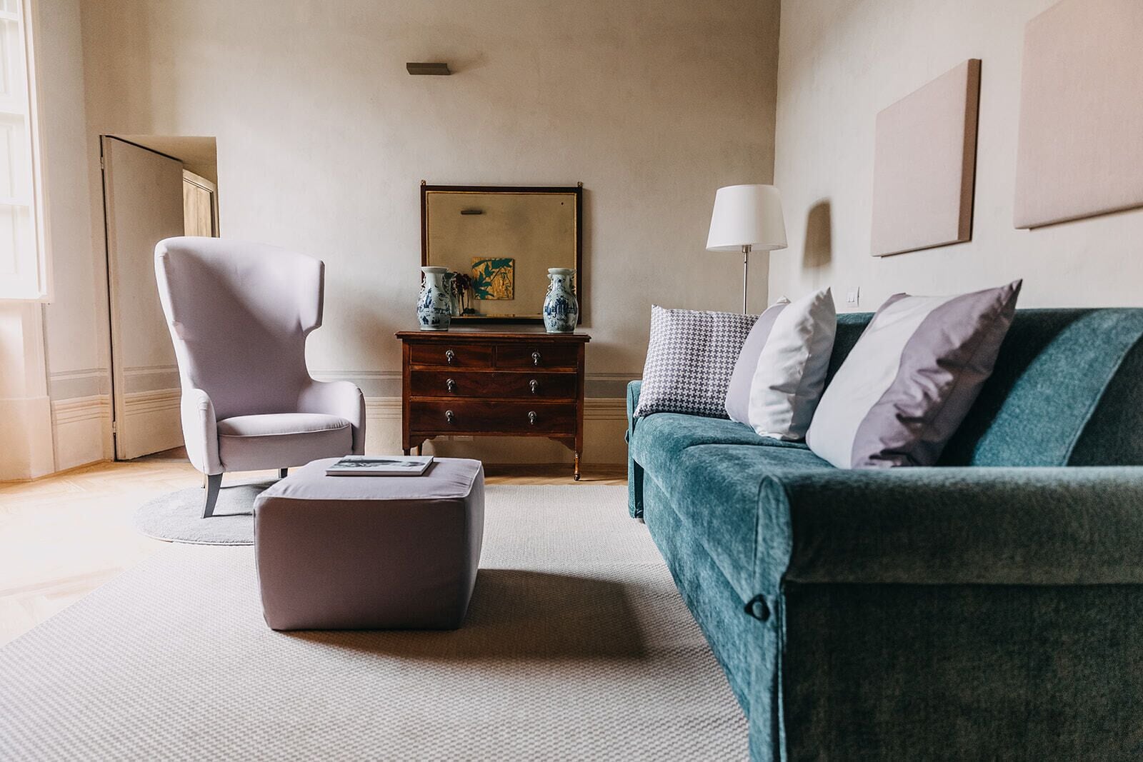 Un salon moderne avec un fauteuil gris, un canapé turquoise, une table d’appoint en bois et un lampadaire.