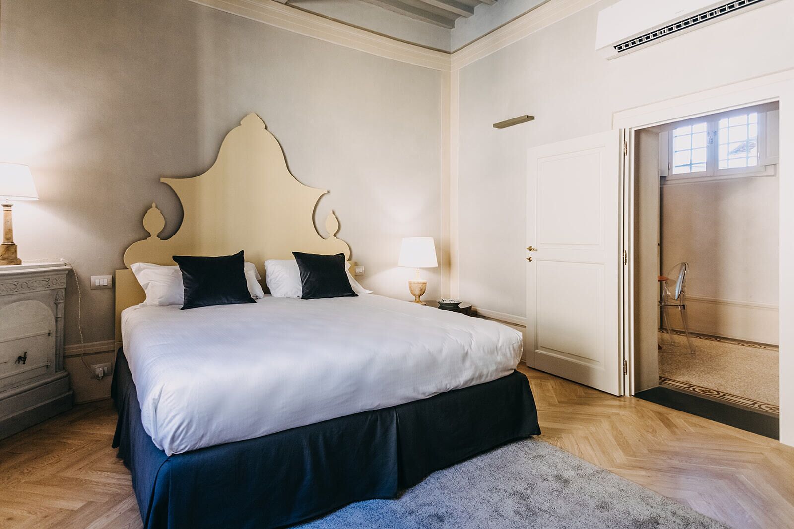Un dormitorio con una cama grande, mesitas de noche, una mesita auxiliar, una puerta y una ventana.