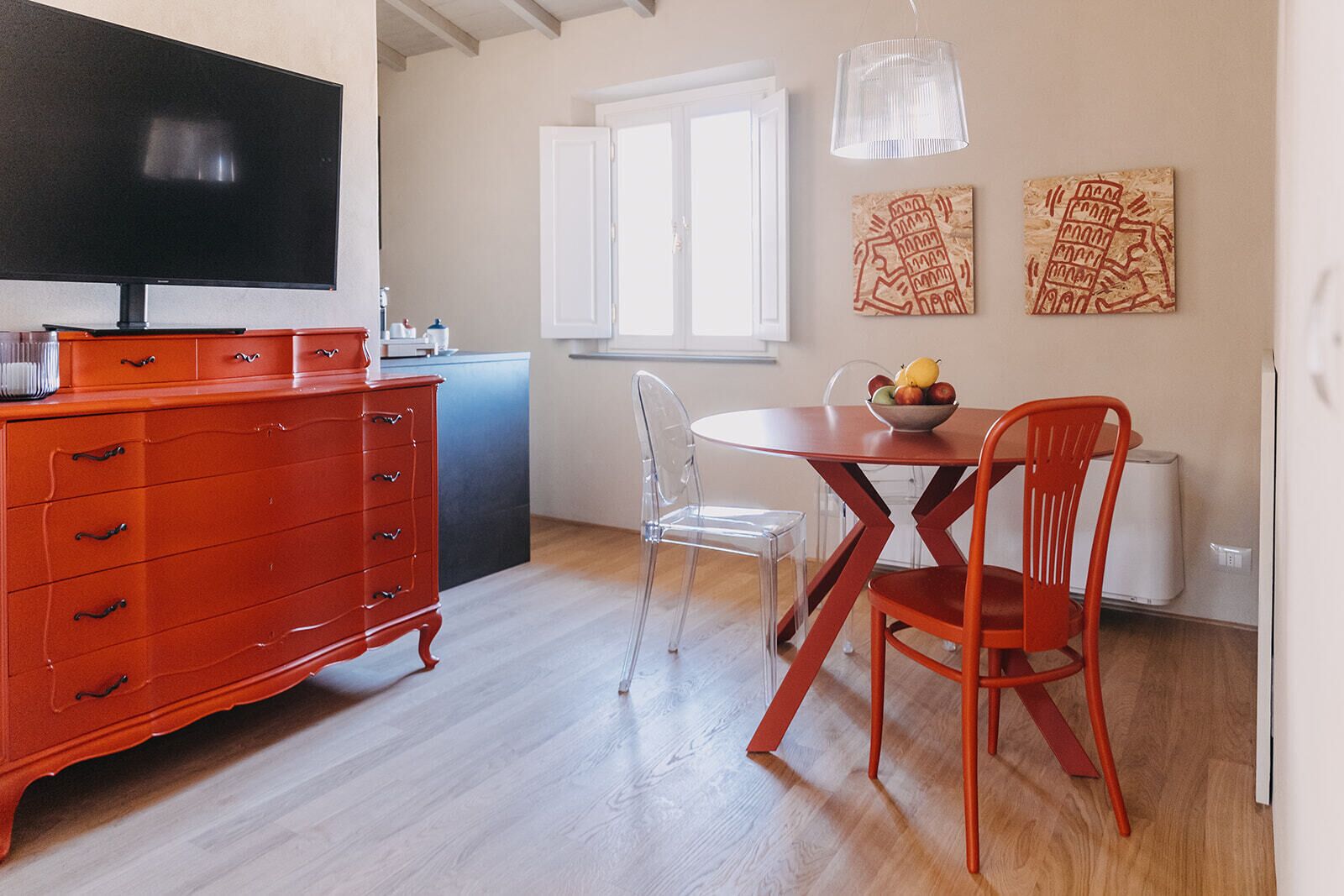 A modern kitchen with a red cabinet, a dining table with chairs, and a TV mounted on the wall.