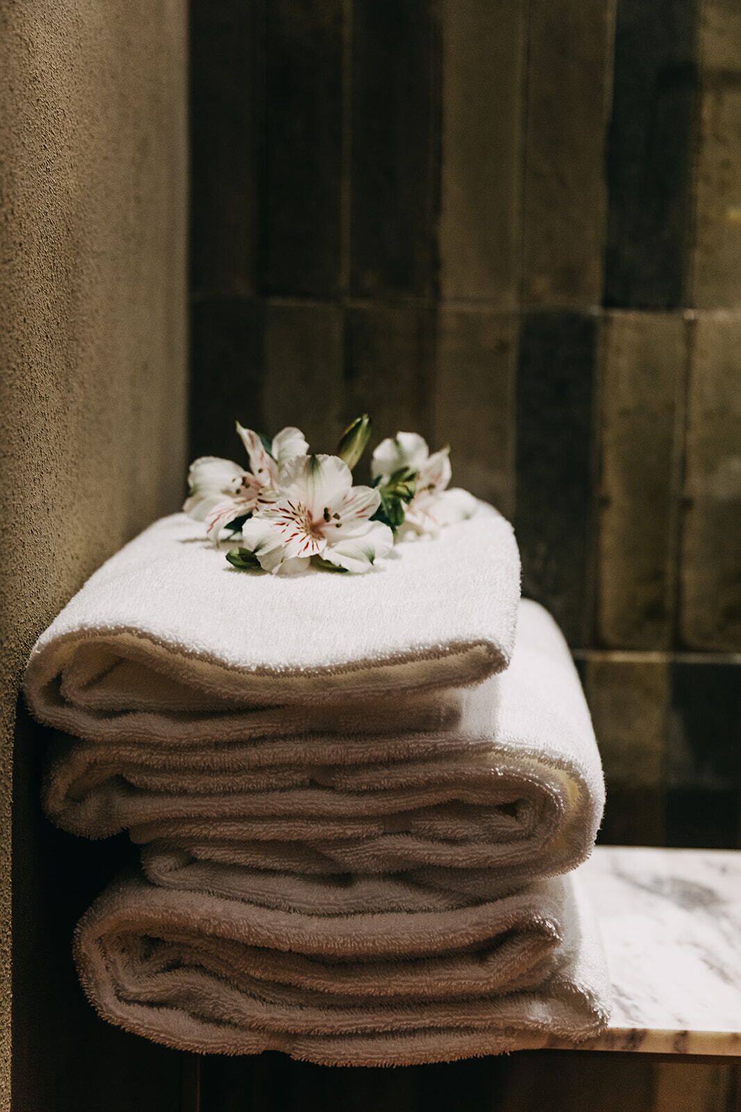 A stack of folded towels on a shelf with a floral arrangement on top.
