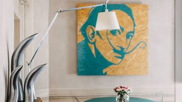 Une pièce avec une table de couleur turquoise, une lampe blanche, une œuvre d’art encadrée et un vase rempli de fleurs.