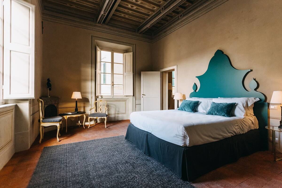 A bedroom with a large bed, a window, a chair, and a small table.